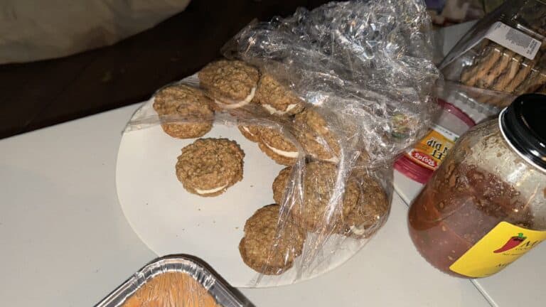Golden Oreo cookie sandwiches with cream filling, packaged in a clear plastic bag, placed on a white surface with various food items and condiments in the background.