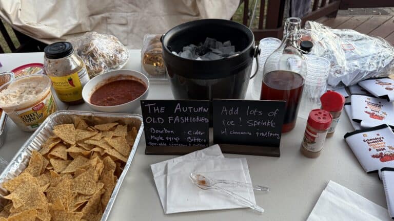Festive autumn-themed party table with snacks and drinks, featuring signs with recipes, hot cider, corn dip, and tortilla chips, perfect for holiday gatherings and seasonal celebrations.