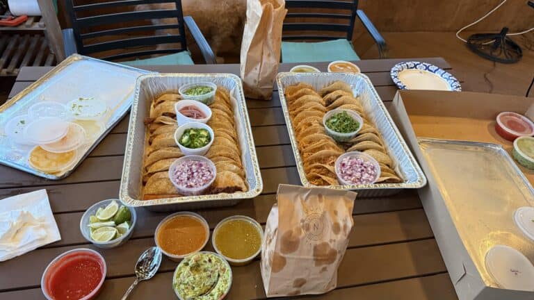 Freshly prepared tacos with various toppings and sides on a wooden table, showcasing authentic Mexican cuisine, including lime wedges, salsas, and condiments for a delicious meal.